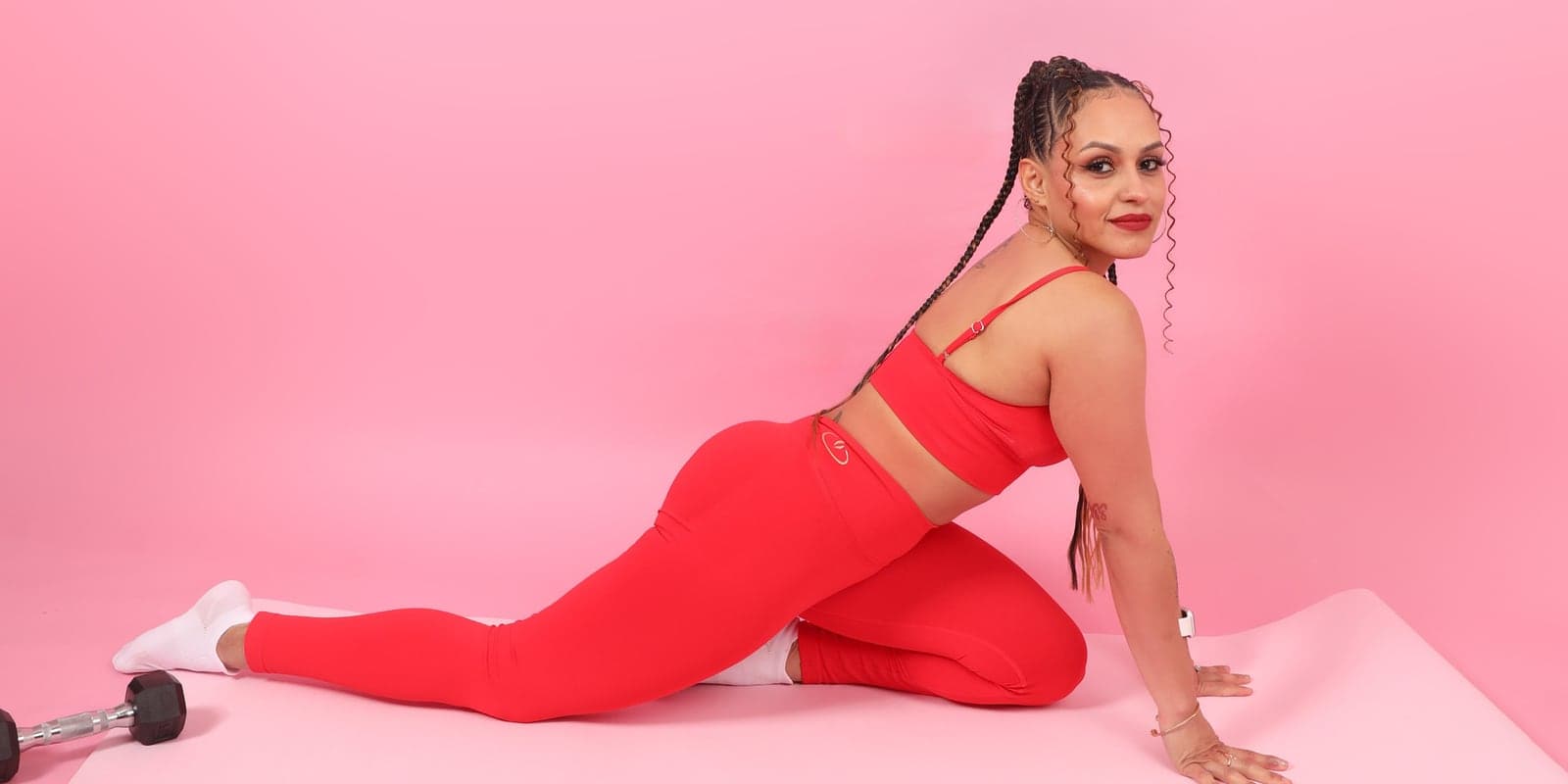 Woman in the red AEVAH set stretching on a mat, pink backdrop